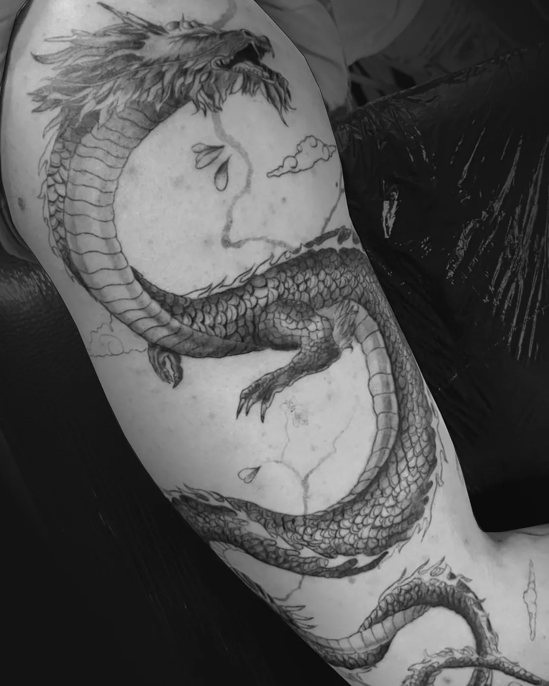 Realistic-Tattoo: asiatischer Drache mit fein schattierten Schuppen, der sich um Schulter und Oberarm windet